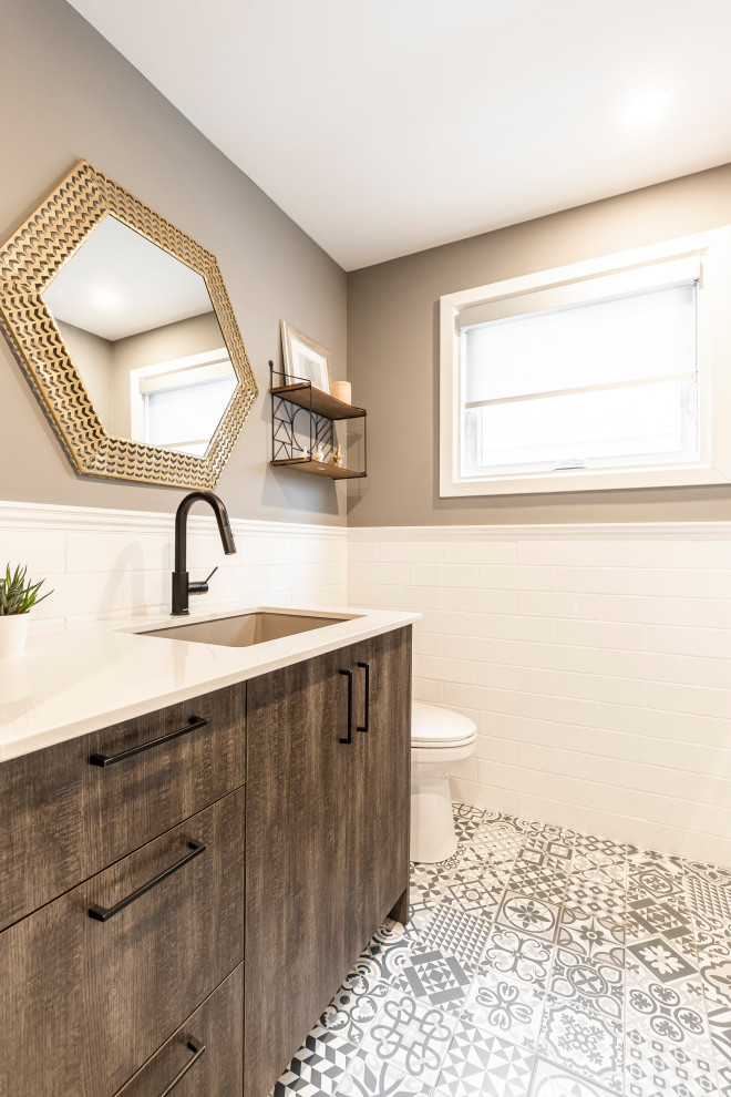 Mid-sized cottage single-wall ceramic tile and multicolored floor utility room photo in Montreal with an undermount sink, flat-panel cabinets, dark wood cabinets, quartz countertops, white backsplash, subway tile backsplash, gray walls, a stacked washer/dryer and white countertops