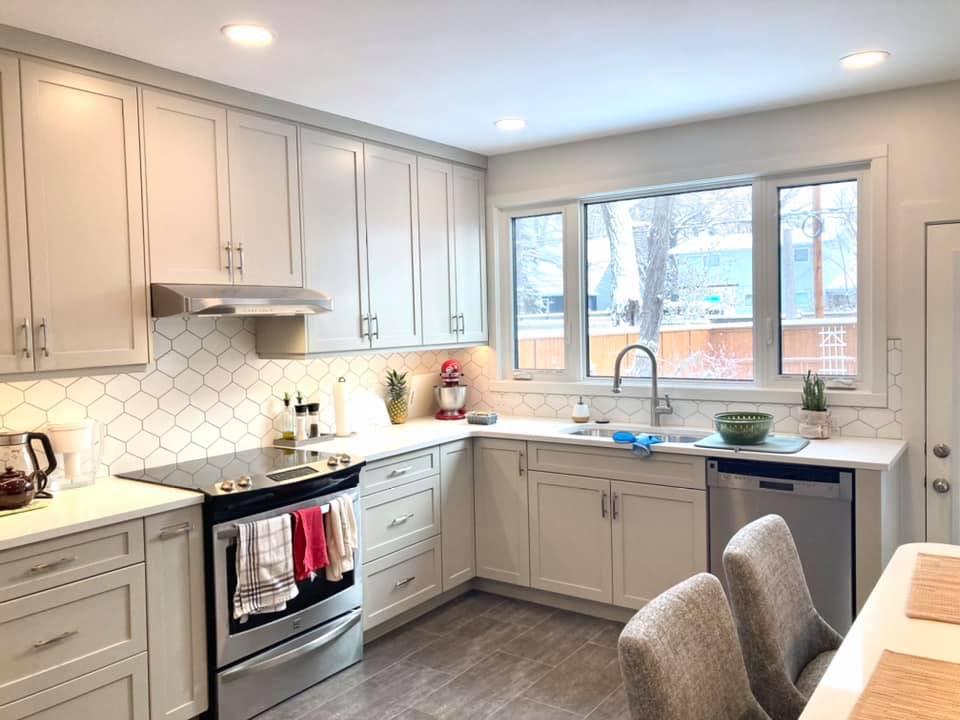 Example of a mid-sized transitional u-shaped vinyl floor and gray floor enclosed kitchen design with an undermount sink, shaker cabinets, beige cabinets, quartz countertops, white backsplash, ceramic backsplash, stainless steel appliances and white countertops