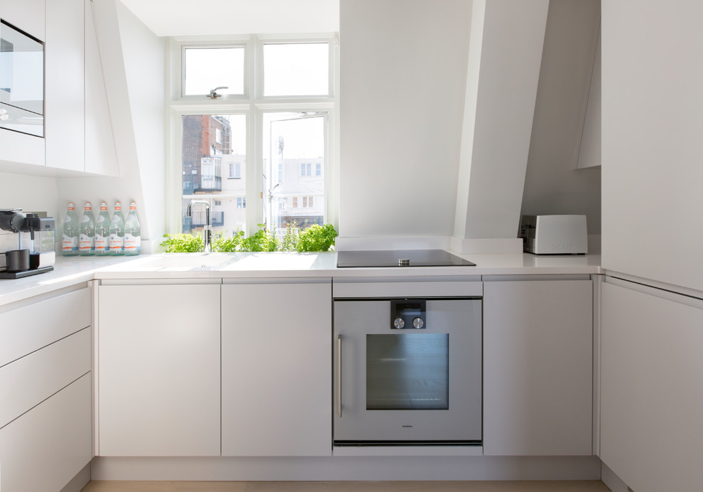 Contemporary u-shaped kitchen in London with an integrated sink, flat-panel cabinets, white cabinets and white benchtop.