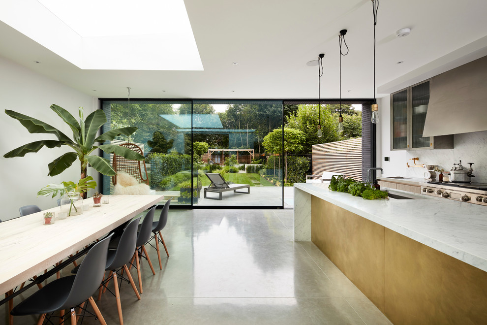 Contemporary open plan kitchen in London with marble benchtops, white splashback and concrete floors.