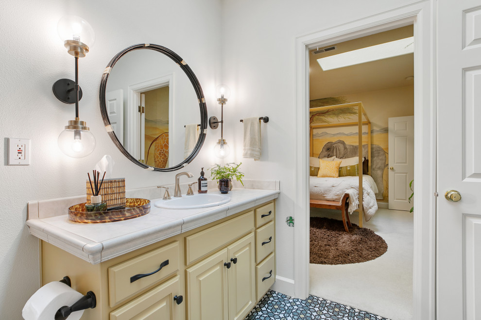 Inspiration for a mid-sized eclectic 3/4 bathroom in Portland with raised-panel cabinets, yellow cabinets, an alcove tub, a shower/bathtub combo, a one-piece toilet, multi-coloured tile, ceramic tile, white walls, porcelain floors, a drop-in sink, tile benchtops, multi-coloured floor, a shower curtain, beige benchtops, a single vanity, a built-in vanity and vaulted.