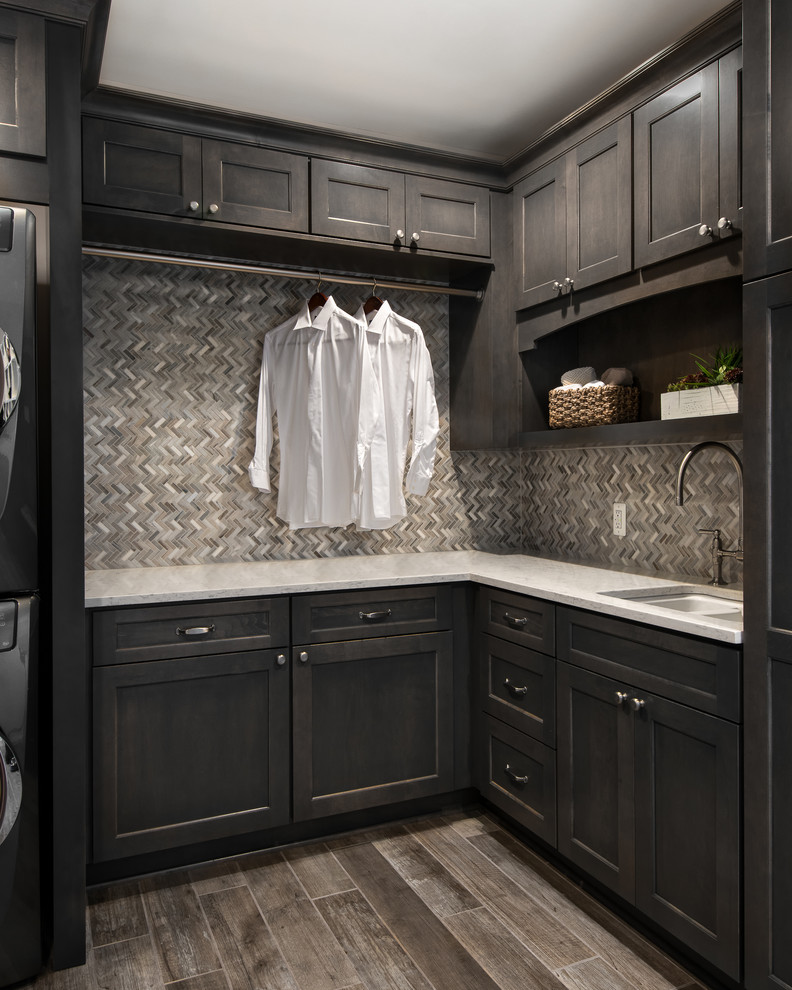 Design ideas for a mid-sized transitional l-shaped laundry room in Detroit with an undermount sink, flat-panel cabinets, dark wood cabinets, quartz benchtops, beige walls, porcelain floors and a stacked washer and dryer.