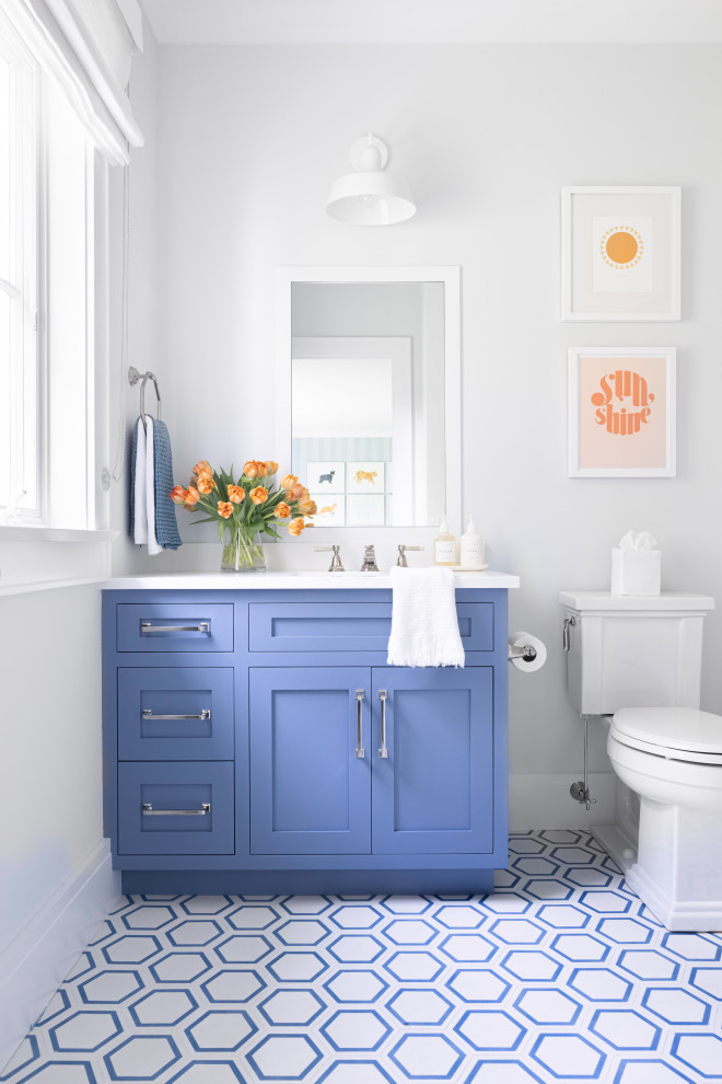 Mid-sized traditional kids bathroom in New York with recessed-panel cabinets, blue cabinets, a corner tub, a shower/bathtub combo, a one-piece toilet, white tile, ceramic tile, white walls, cement tiles, an integrated sink, marble benchtops, blue floor, a shower curtain and white benchtops.