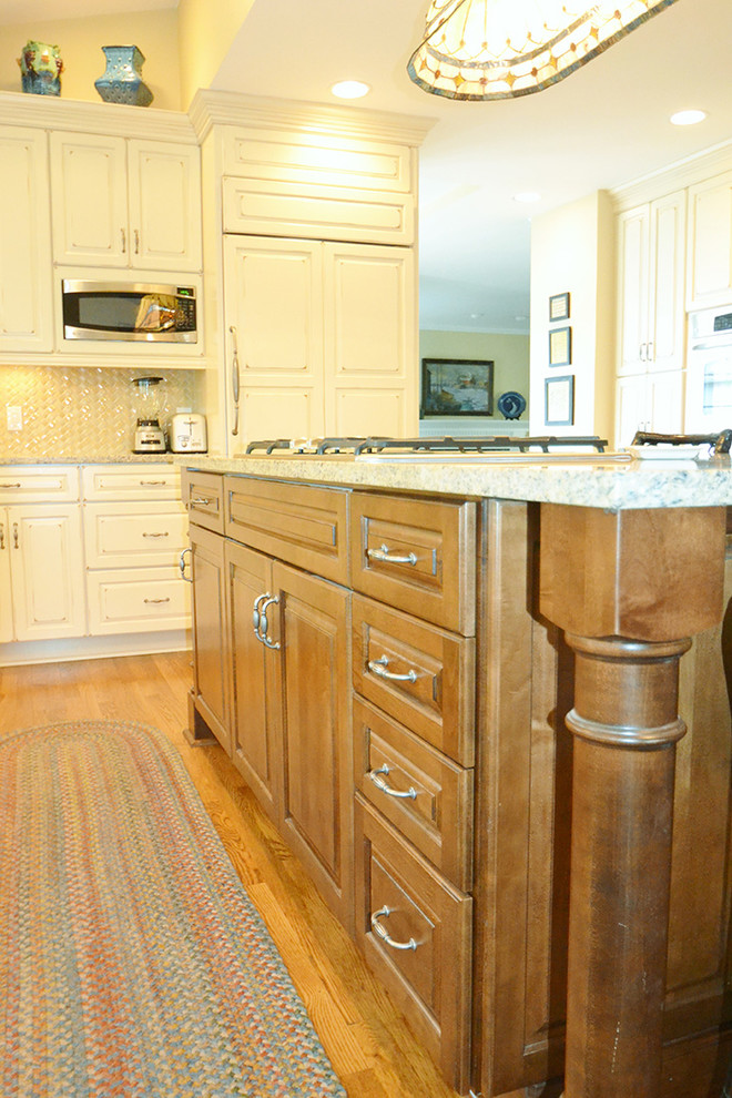 Large transitional l-shaped medium tone wood floor eat-in kitchen photo in Columbus with an undermount sink, raised-panel cabinets, beige cabinets, granite countertops, beige backsplash, paneled appliances and an island