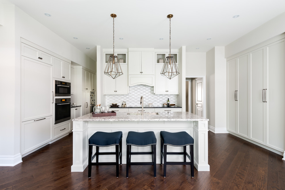 Photo of an expansive transitional kitchen in Toronto with an undermount sink, shaker cabinets, quartz benchtops, white splashback, porcelain splashback, stainless steel appliances, dark hardwood floors, with island and white cabinets.