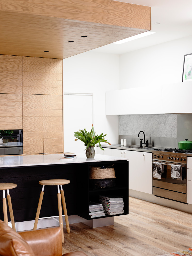 Inspiration for a large contemporary eat-in kitchen in Auckland with a double-bowl sink, white cabinets, stainless steel benchtops, grey splashback, stone slab splashback, stainless steel appliances and brown floor.
