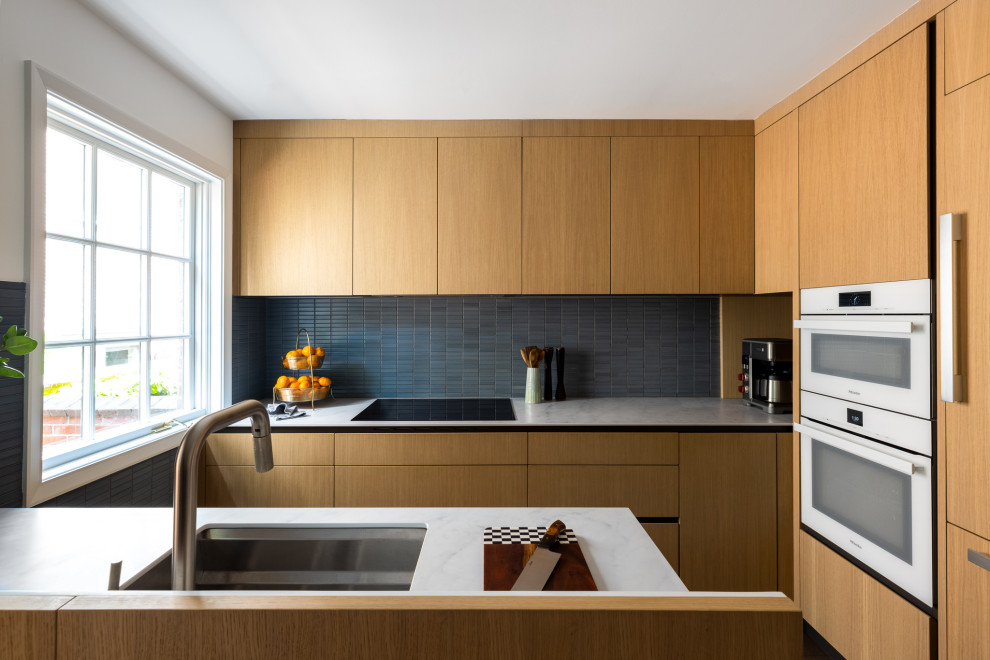 Пример оригинального дизайна: кухня в современном стиле с плоскими фасадами, фасадами цвета дерева среднего тона, синим фартуком, техникой под мебельный фасад и белой столешницей