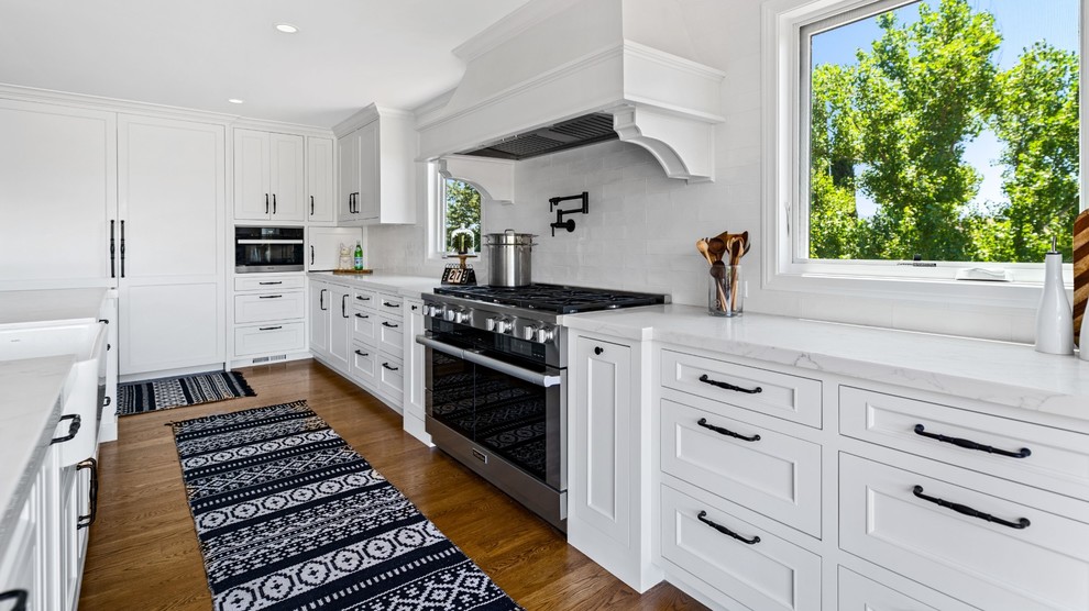 Inspiration for a large transitional single-wall medium tone wood floor and brown floor eat-in kitchen remodel with a single-bowl sink, raised-panel cabinets, white cabinets, quartzite countertops, white backsplash, ceramic backsplash, stainless steel appliances, an island and white countertops