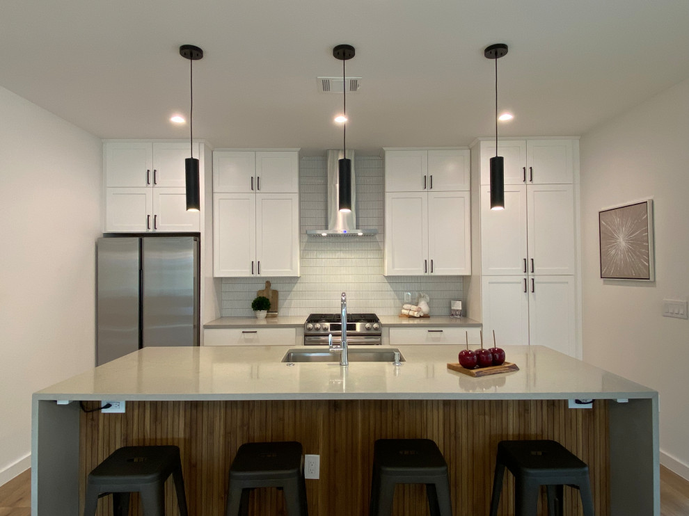 Open concept kitchen - galley open concept kitchen idea in Austin with an undermount sink, shaker cabinets, white cabinets, quartz countertops, white backsplash, ceramic backsplash, stainless steel appliances, an island and gray countertops