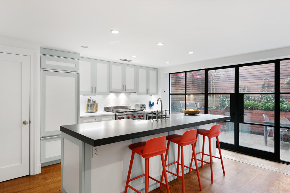 Mid-sized transitional kitchen in New York with white splashback, medium hardwood floors, with island, granite benchtops, ceramic splashback, shaker cabinets and panelled appliances.