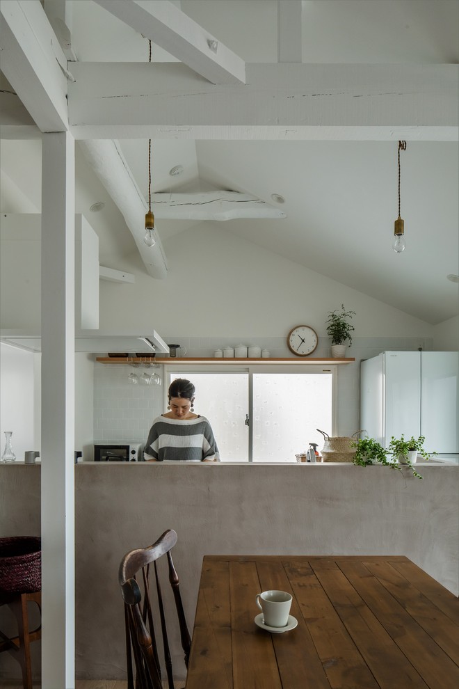 This is an example of a small traditional single-wall open plan kitchen in Other with an integrated sink, beaded inset cabinets, white cabinets, stainless steel benchtops, white splashback, ceramic splashback, black appliances, light hardwood floors, with island, white floor and grey benchtop.