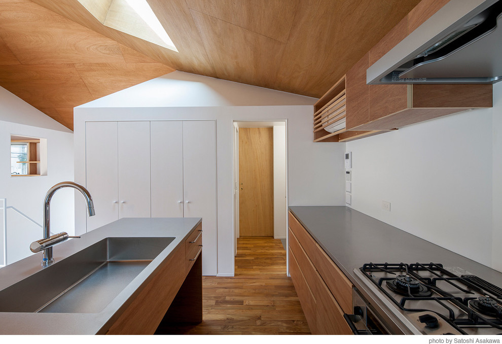 This is an example of a mid-sized contemporary galley open plan kitchen in Tokyo with flat-panel cabinets, medium wood cabinets, stainless steel benchtops, white splashback, stainless steel appliances, medium hardwood floors and with island.
