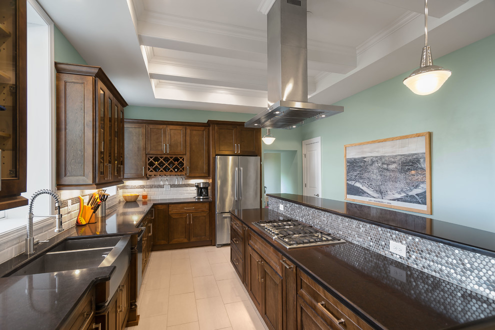 Photo of a mid-sized eclectic l-shaped separate kitchen in Cincinnati with a farmhouse sink, shaker cabinets, dark wood cabinets, solid surface benchtops, metallic splashback, mosaic tile splashback, stainless steel appliances, porcelain floors and with island.