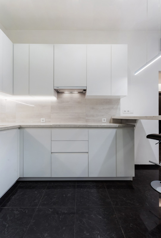 This is an example of a mid-sized contemporary l-shaped open plan kitchen in Moscow with an integrated sink, flat-panel cabinets, white cabinets, quartz benchtops, grey splashback, porcelain splashback, white appliances, porcelain floors, black floor and white benchtop.