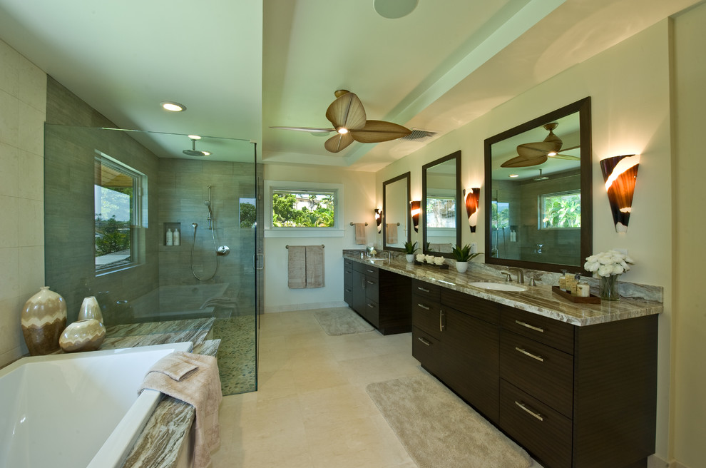 This is an example of a large tropical master bathroom in Hawaii with an undermount sink, flat-panel cabinets, dark wood cabinets, granite benchtops, a drop-in tub, a corner shower, green walls, travertine floors, gray tile, beige floor and a hinged shower door.