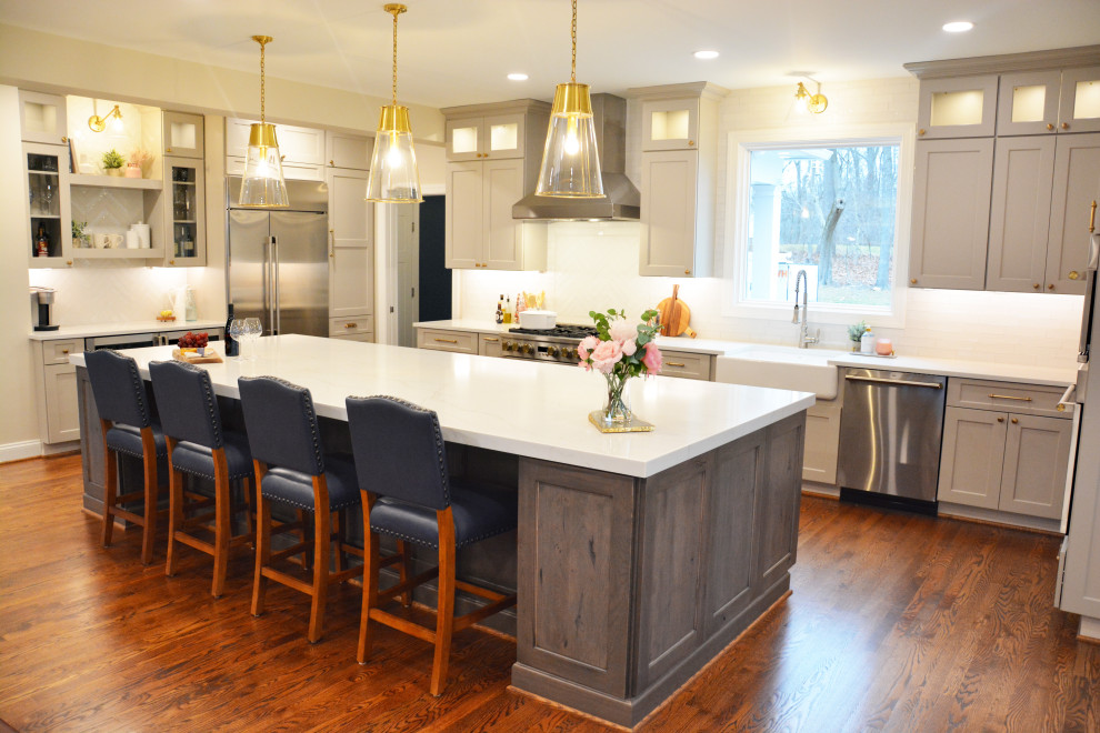 Large classic l-shaped kitchen/diner in Baltimore with a belfast sink, recessed-panel cabinets, grey cabinets, engineered stone countertops, white splashback, stainless steel appliances, dark hardwood flooring, an island, brown floors and white worktops.
