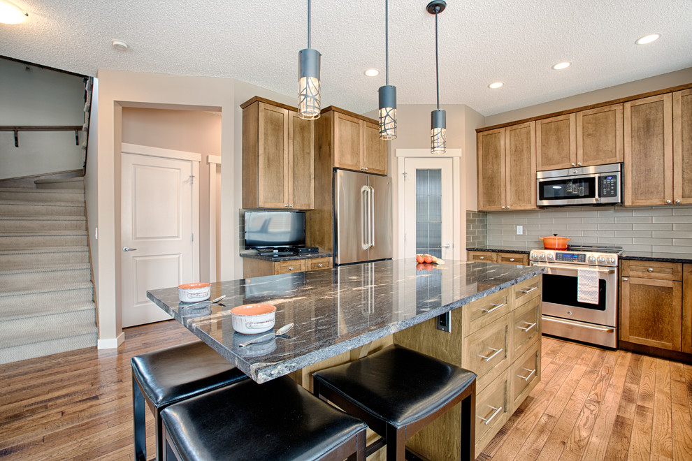 Mid-sized mountain style u-shaped medium tone wood floor and brown floor eat-in kitchen photo in Calgary with an undermount sink, shaker cabinets, medium tone wood cabinets, granite countertops, gray backsplash, glass tile backsplash, stainless steel appliances and an island