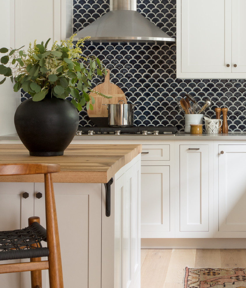 This is an example of a beach style kitchen in Boston with a farmhouse sink, shaker cabinets, white cabinets, wood benchtops, blue splashback, ceramic splashback and light hardwood floors.