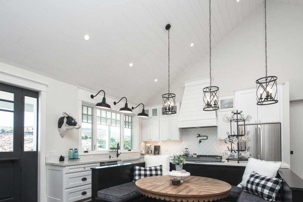 Large country l-shaped open plan kitchen in Los Angeles with a farmhouse sink, shaker cabinets, white cabinets, quartz benchtops, white splashback, ceramic splashback, stainless steel appliances, dark hardwood floors, with island, brown floor and white benchtop.