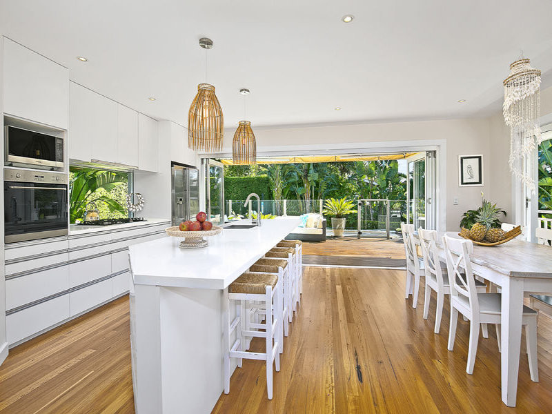 Design ideas for a beach style galley kitchen in Sydney with an undermount sink, quartz benchtops, glass sheet splashback, stainless steel appliances, light hardwood floors, with island, beaded inset cabinets and white cabinets.