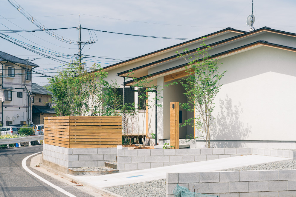 Cette image montre une façade de maison blanche asiatique de plain-pied avec un toit à deux pans, un toit en métal et un toit noir.