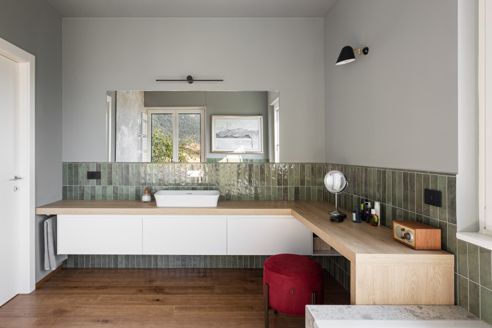 На фото: большая главная ванная комната в современном стиле с плоскими фасадами, белыми фасадами, накладной ванной, инсталляцией, зеленой плиткой, удлиненной плиткой, зелеными стенами, паркетным полом среднего тона, настольной раковиной, столешницей из дерева, бежевым полом, бежевой столешницей, тумбой под одну раковину и подвесной тумбой