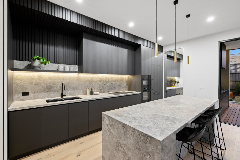 This is an example of a mid-sized contemporary galley eat-in kitchen in Melbourne with a double-bowl sink, dark wood cabinets, marble benchtops, grey splashback, marble splashback, black appliances, light hardwood floors, with island and grey benchtop.