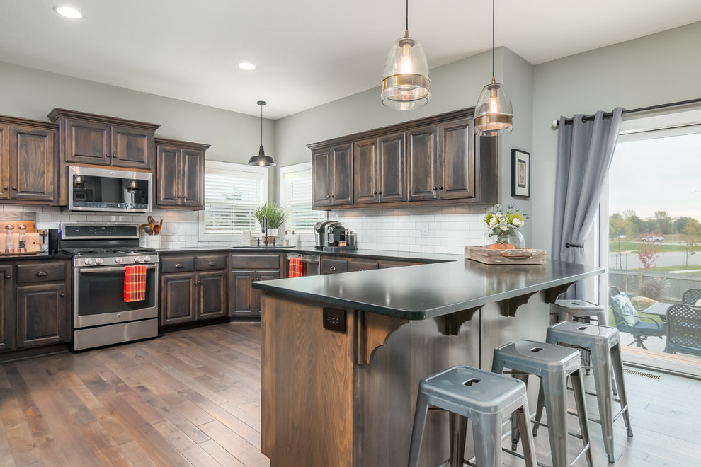 Kitchen - traditional u-shaped medium tone wood floor and brown floor kitchen idea in Kansas City with raised-panel cabinets, dark wood cabinets, white backsplash, subway tile backsplash, black appliances and a peninsula
