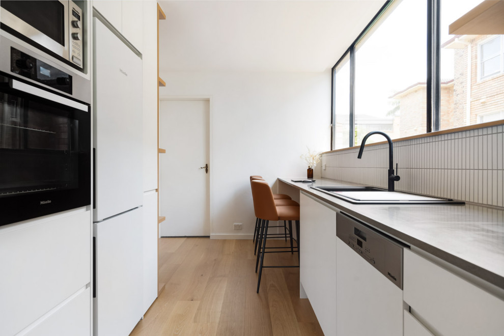 Idéer för ett avskilt modernt u-kök, med en enkel diskho, vita skåp, bänkskiva i kvarts, vitt stänkskydd, stänkskydd i keramik, mellanmörkt trägolv och brunt golv