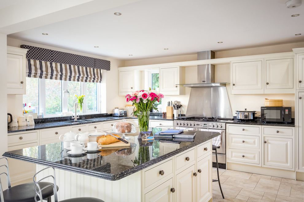 This is an example of a large l-shaped separate kitchen in Gloucestershire with an undermount sink, beaded inset cabinets, granite benchtops, metallic splashback, metal splashback, stainless steel appliances, ceramic floors, with island and beige cabinets.