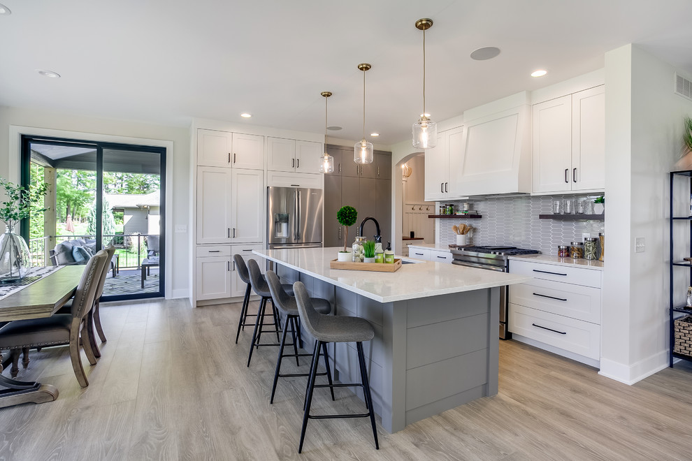 Photo of a transitional eat-in kitchen in Grand Rapids with an undermount sink, shaker cabinets, white cabinets, grey splashback, stainless steel appliances, light hardwood floors, with island, beige floor and white benchtop.