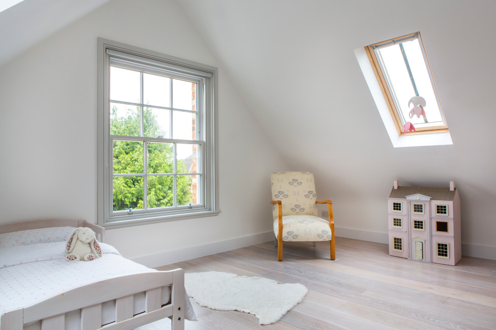 Photo of a scandinavian toddler room for girls in London with white walls and light hardwood floors.