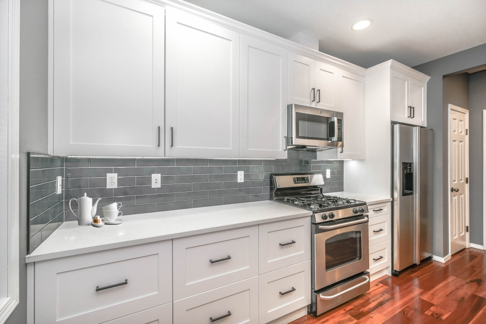 Photo of a mid-sized modern single-wall kitchen pantry in Seattle with an undermount sink, shaker cabinets, white cabinets, quartzite benchtops, grey splashback, porcelain splashback, stainless steel appliances, medium hardwood floors, with island, brown floor, white benchtop and coffered.