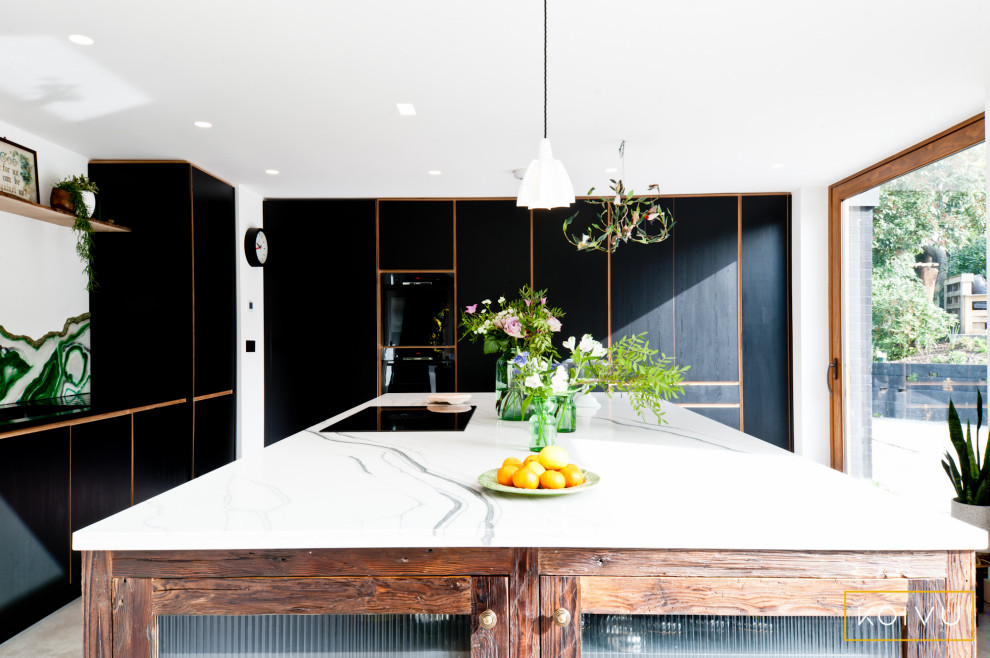 Mid-sized contemporary l-shaped open plan kitchen in Kent with a drop-in sink, flat-panel cabinets, black cabinets, green splashback, glass sheet splashback, black appliances, with island and grey floor.