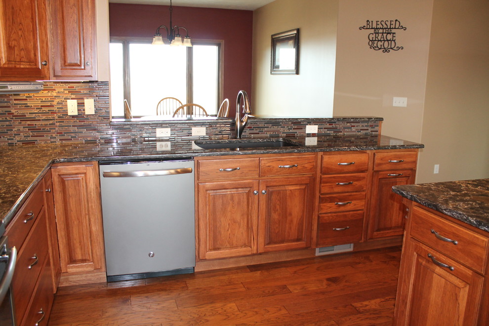 Large l-shaped eat-in kitchen photo with an undermount sink, raised-panel cabinets, medium tone wood cabinets, solid surface countertops, glass tile backsplash, stainless steel appliances, beige walls and an island