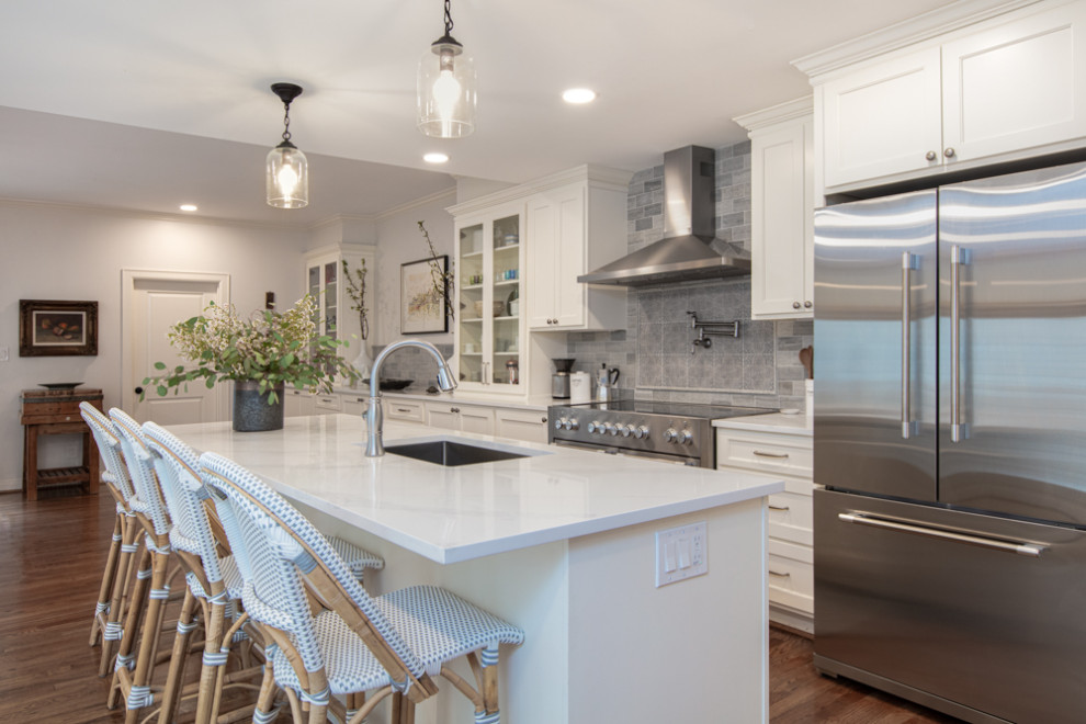 Mid-sized traditional single-wall eat-in kitchen in Houston with a drop-in sink, shaker cabinets, white cabinets, quartz benchtops, grey splashback, stone tile splashback, stainless steel appliances, medium hardwood floors, with island, multi-coloured floor and white benchtop.