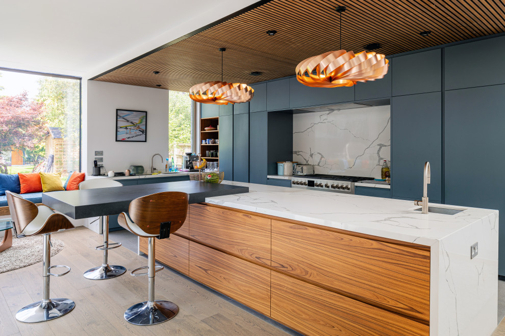 Inspiration for a contemporary l-shaped kitchen in Surrey with a submerged sink, flat-panel cabinets, blue cabinets, white splashback, stone slab splashback, stainless steel appliances, an island, grey floors, white worktops and a wood ceiling.