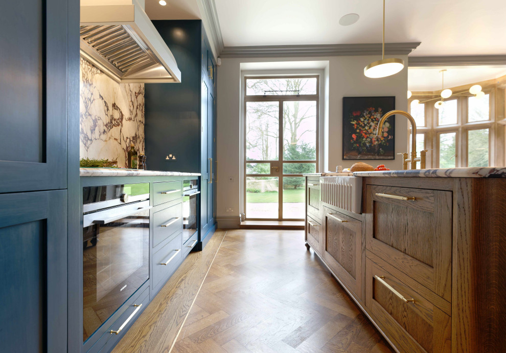 Design ideas for an expansive traditional galley open plan kitchen in London with a farmhouse sink, shaker cabinets, blue cabinets, marble benchtops, multi-coloured splashback, marble splashback, stainless steel appliances, medium hardwood floors, with island, brown floor and multi-coloured benchtop.