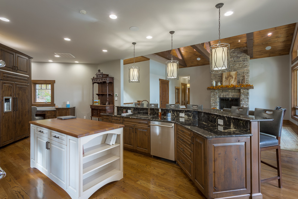 Inspiration for a large country l-shaped open plan kitchen in Charlotte with raised-panel cabinets, dark wood cabinets, granite benchtops, stone slab splashback, stainless steel appliances, medium hardwood floors, multiple islands, a double-bowl sink, beige splashback and brown floor.
