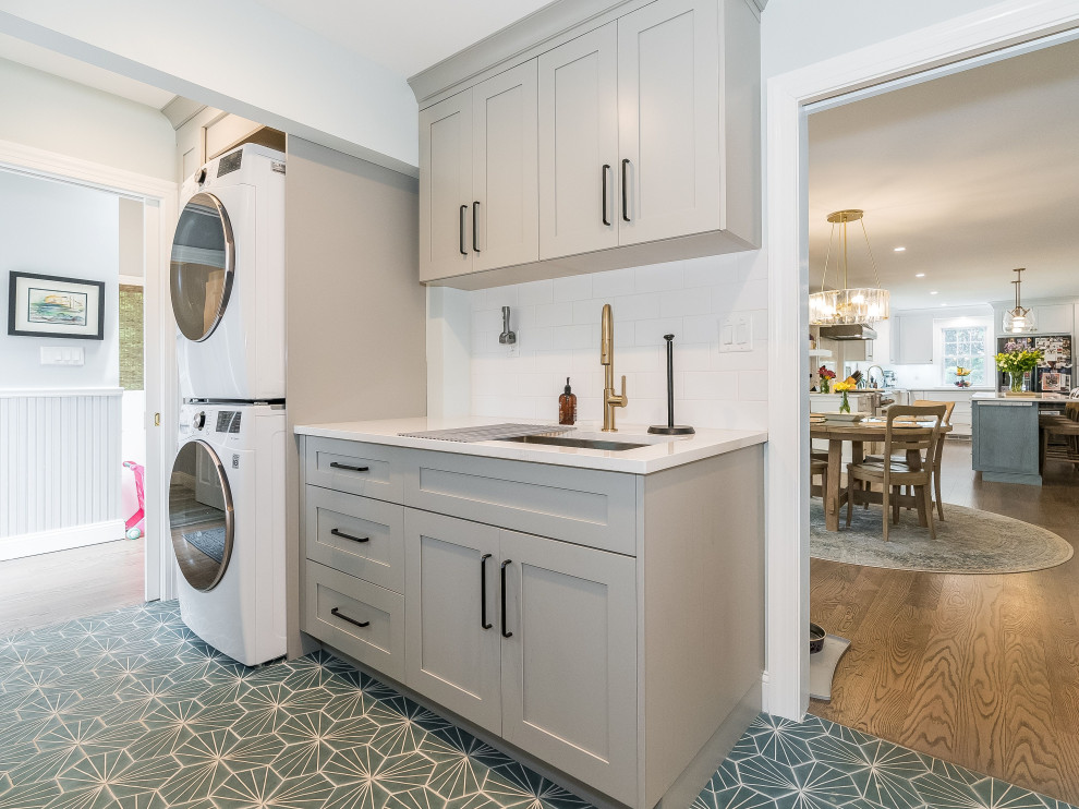 This is an example of a mid-sized galley utility room in New York with an undermount sink, shaker cabinets, grey cabinets, quartz benchtops, white splashback, ceramic splashback, blue walls, porcelain floors, a stacked washer and dryer, blue floor and white benchtop.