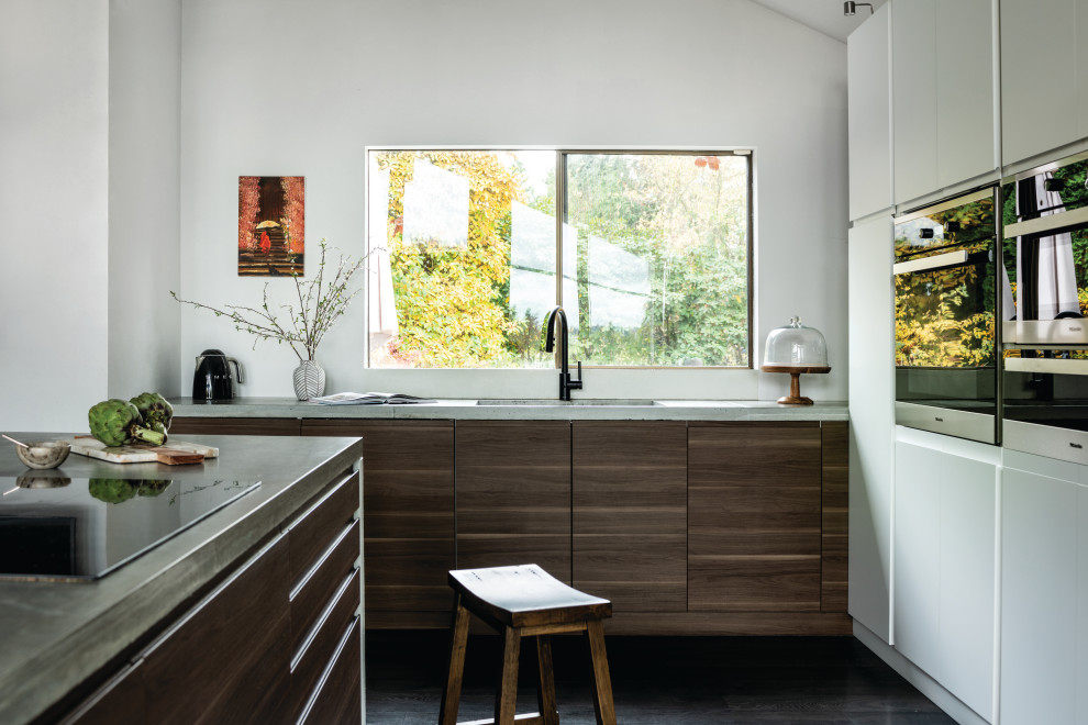 Photo of a medium sized contemporary l-shaped kitchen/diner in Seattle with a submerged sink, flat-panel cabinets, white cabinets, concrete worktops, stainless steel appliances, laminate floors, an island, black floors, grey worktops and a vaulted ceiling.