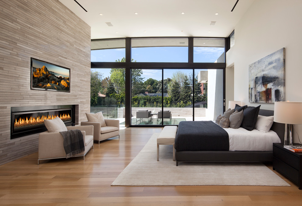 Inspiration for an expansive contemporary master bedroom in Los Angeles with a ribbon fireplace, a stone fireplace surround, white walls, light hardwood floors and brown floor.