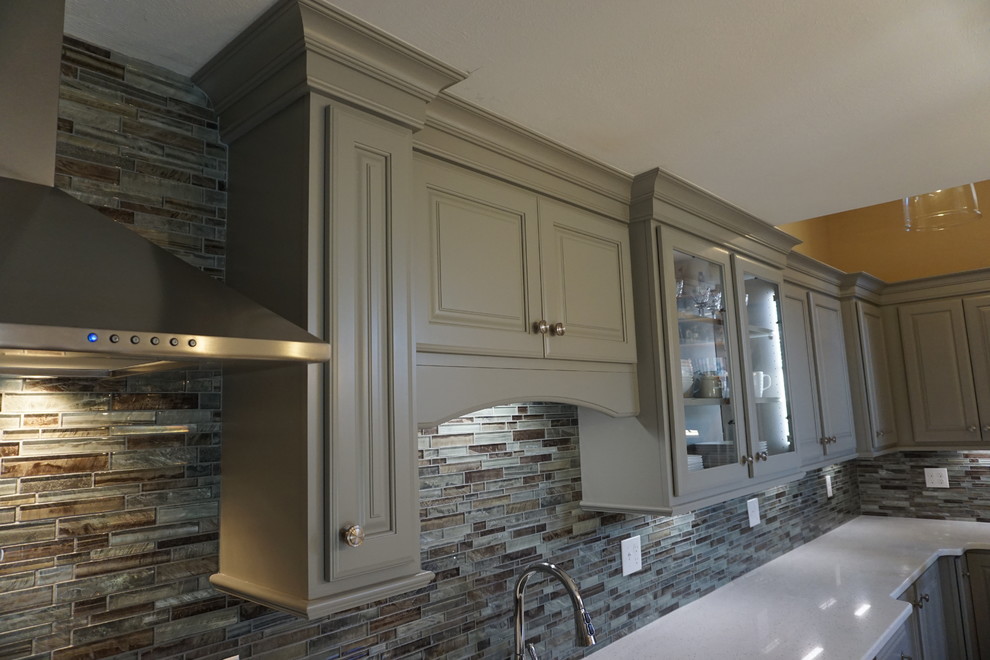 Small elegant l-shaped medium tone wood floor eat-in kitchen photo in Providence with a triple-bowl sink, raised-panel cabinets, gray cabinets, quartz countertops, gray backsplash, mosaic tile backsplash, stainless steel appliances, an island and white countertops