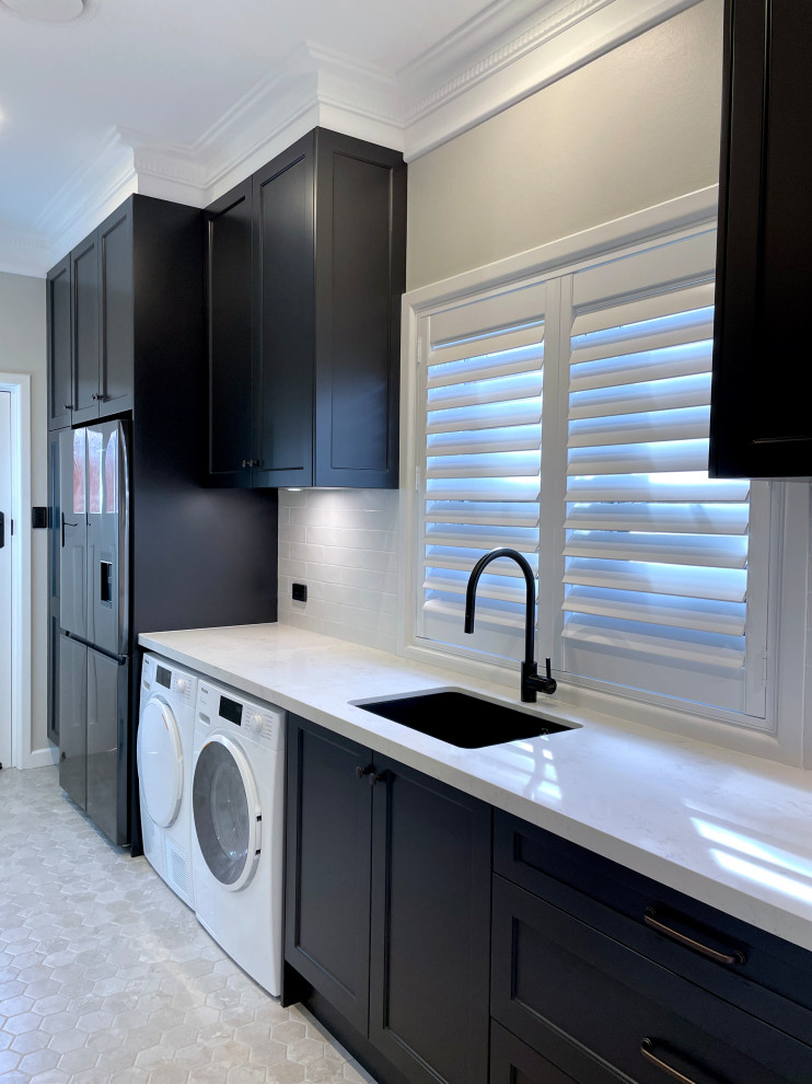 シドニーにあるラグジュアリーな広いトラディショナルスタイルのおしゃれな洗濯室 (I型、アンダーカウンターシンク、落し込みパネル扉のキャビネット、黒いキャビネット、クオーツストーンカウンター、白いキッチンパネル、サブウェイタイルのキッチンパネル、グレーの壁、大理石の床、左右配置の洗濯機・乾燥機、グレーの床、白いキッチンカウンター) の写真