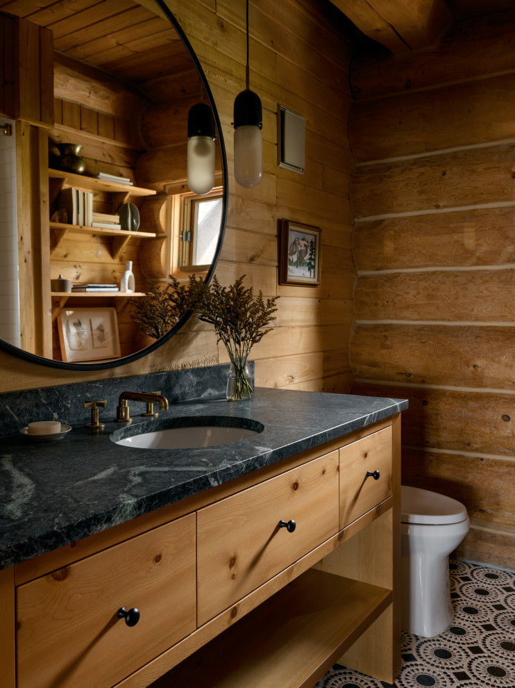 Example of a mountain style mosaic tile floor, multicolored floor and wood wall powder room design in Seattle with flat-panel cabinets, medium tone wood cabinets, brown walls, an undermount sink, black countertops and a freestanding vanity