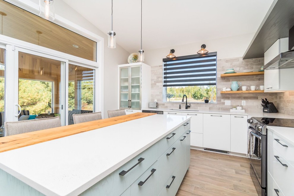 Example of a large transitional l-shaped light wood floor and brown floor kitchen design with an undermount sink, flat-panel cabinets, white cabinets, quartz countertops, brown backsplash, subway tile backsplash, stainless steel appliances and an island