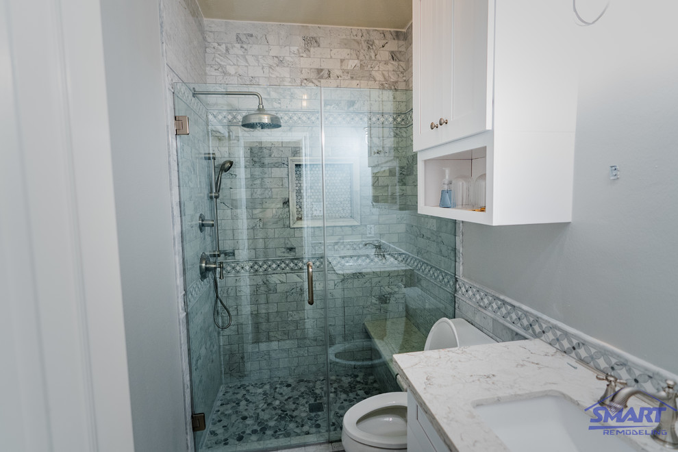 This is an example of a small traditional 3/4 bathroom in Houston with white cabinets, a one-piece toilet, gray tile, grey walls, grey floor, white benchtops, shaker cabinets, an alcove shower, ceramic tile, mosaic tile floors, an undermount sink, marble benchtops, a hinged shower door, a shower seat, a single vanity, a freestanding vanity, coffered and decorative wall panelling.