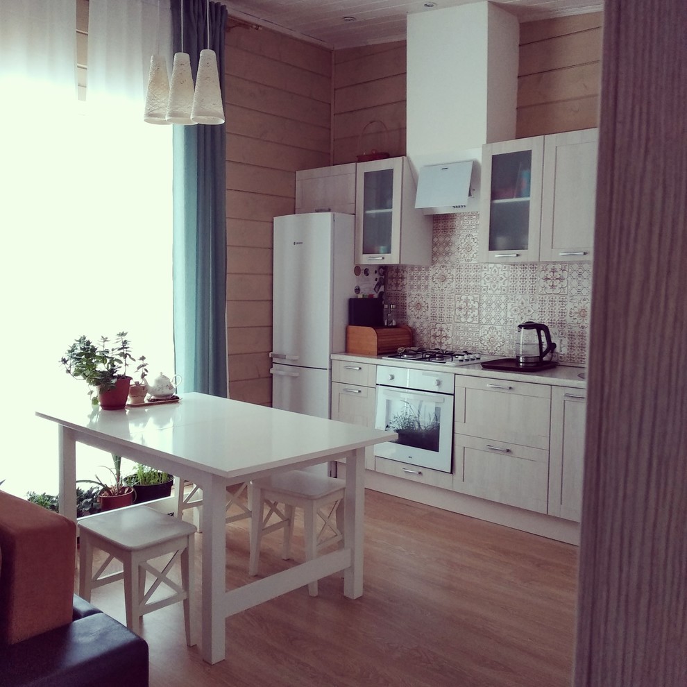 This is an example of a small contemporary single-wall eat-in kitchen in Moscow with glass-front cabinets, beige cabinets, laminate benchtops, multi-coloured splashback, ceramic splashback, white appliances, laminate floors, brown floor, beige benchtop and no island.