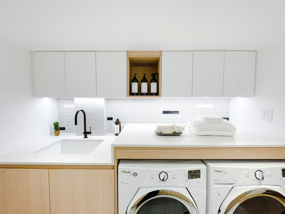 Photo of a large scandinavian galley laundry room in Toronto with an utility sink, flat-panel cabinets, light wood cabinets, quartz benchtops, multi-coloured splashback, porcelain splashback, white walls, ceramic floors, a side-by-side washer and dryer, grey floor and grey benchtop.