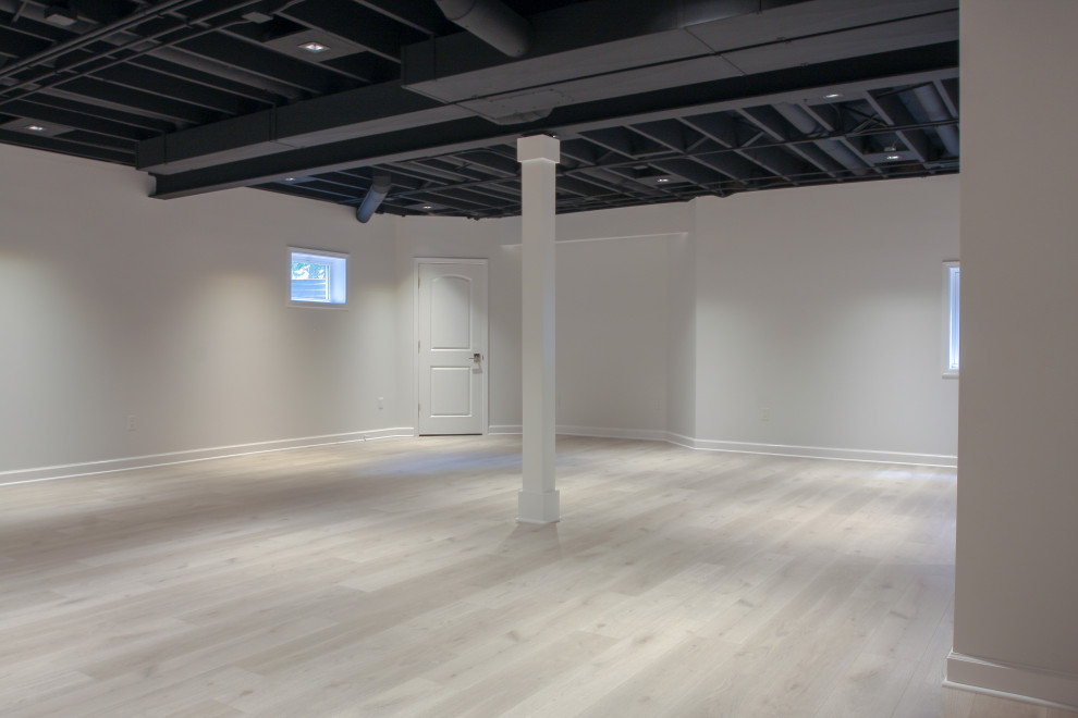 Cette image montre un sous-sol minimaliste enterré et de taille moyenne avec un mur blanc, un sol en vinyl, un sol multicolore et poutres apparentes.